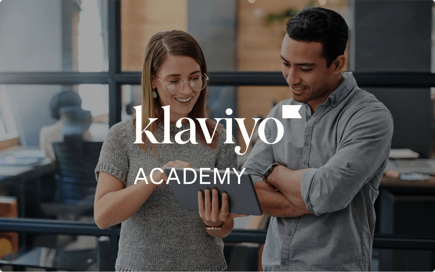 Zwei Mitarbeitende arbeiten gemeinsam auf einem iPad in einem Büro mit Klaviyo-Academy-Text-Overlay
