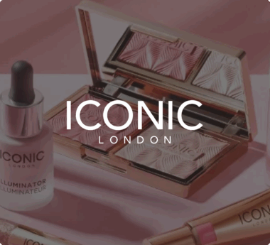Productos de maquillaje de ICONIC London, incluidos una paleta de iluminadores y un iluminador, expuestos sobre una superficie rosa