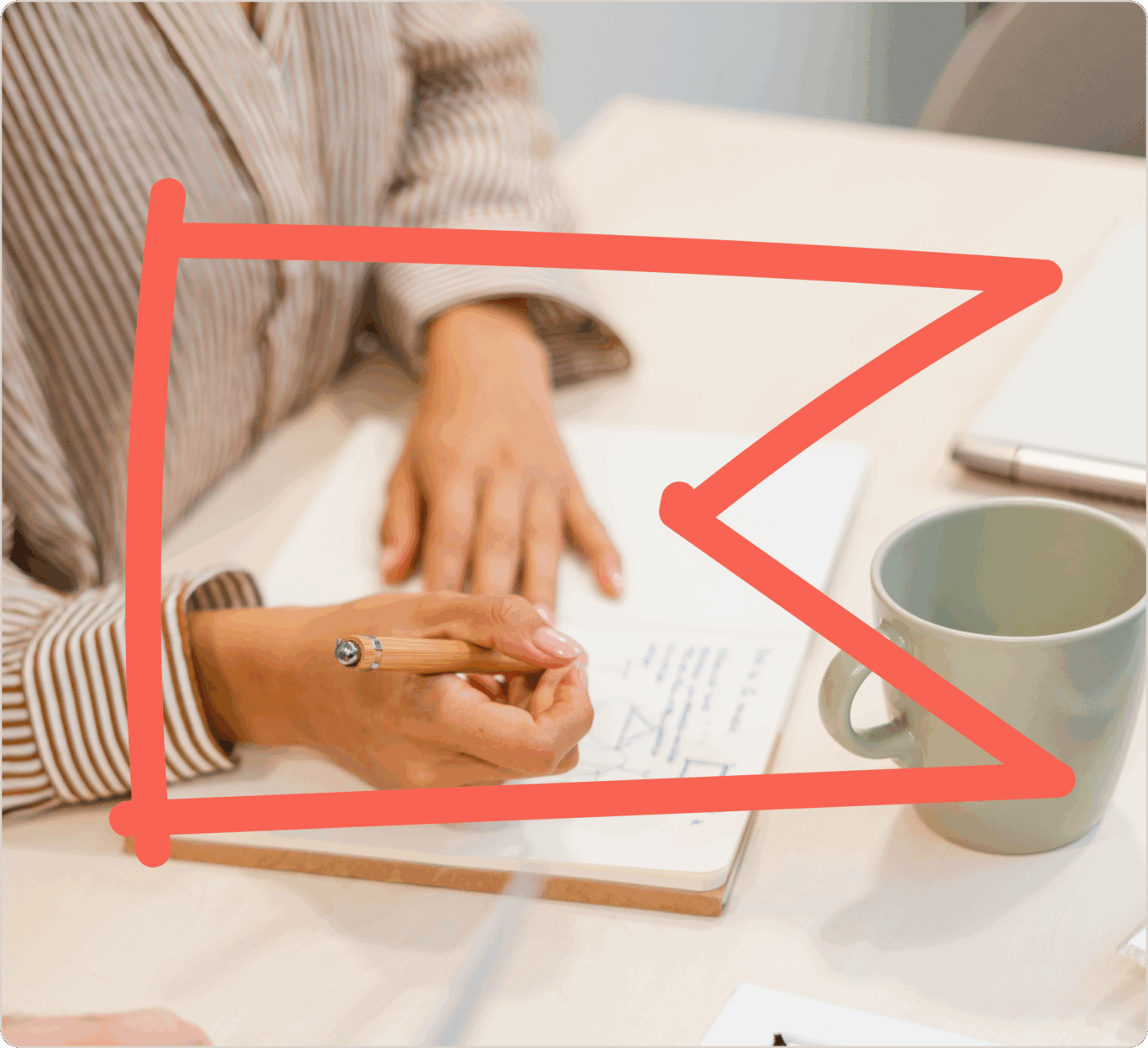 Una persona escribiendo en un cuaderno con un lápiz. Al lado tiene una taza verde sobre una mesa. Se muestra una flecha roja superpuesta que apunta al cuaderno.