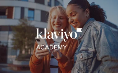 Dos personas sonriendo a un teléfono con la superposición de texto «Klaviyo Academy».