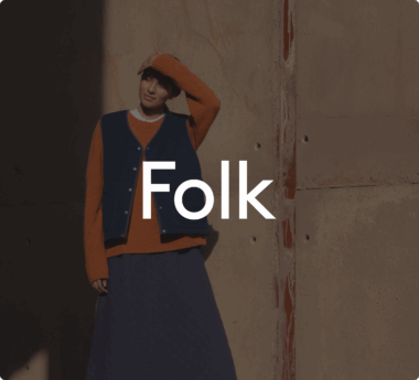 Personne portant un pull orange et un gilet bleu, se tenant contre un mur. Texte "Folk" au centre de l'image.