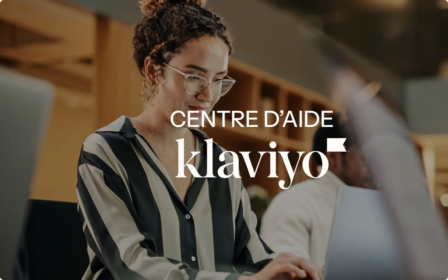 Femme portant des lunettes travaillant sur un ordinateur portable, texte "Centre d'aide Klaviyo" superposé.