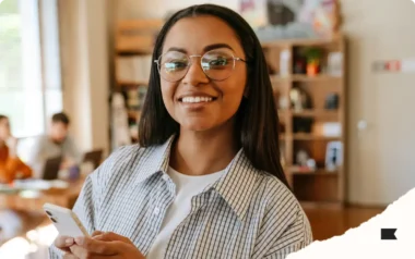 Smiling person with glasses holding a smartphone in a cosy office setting.