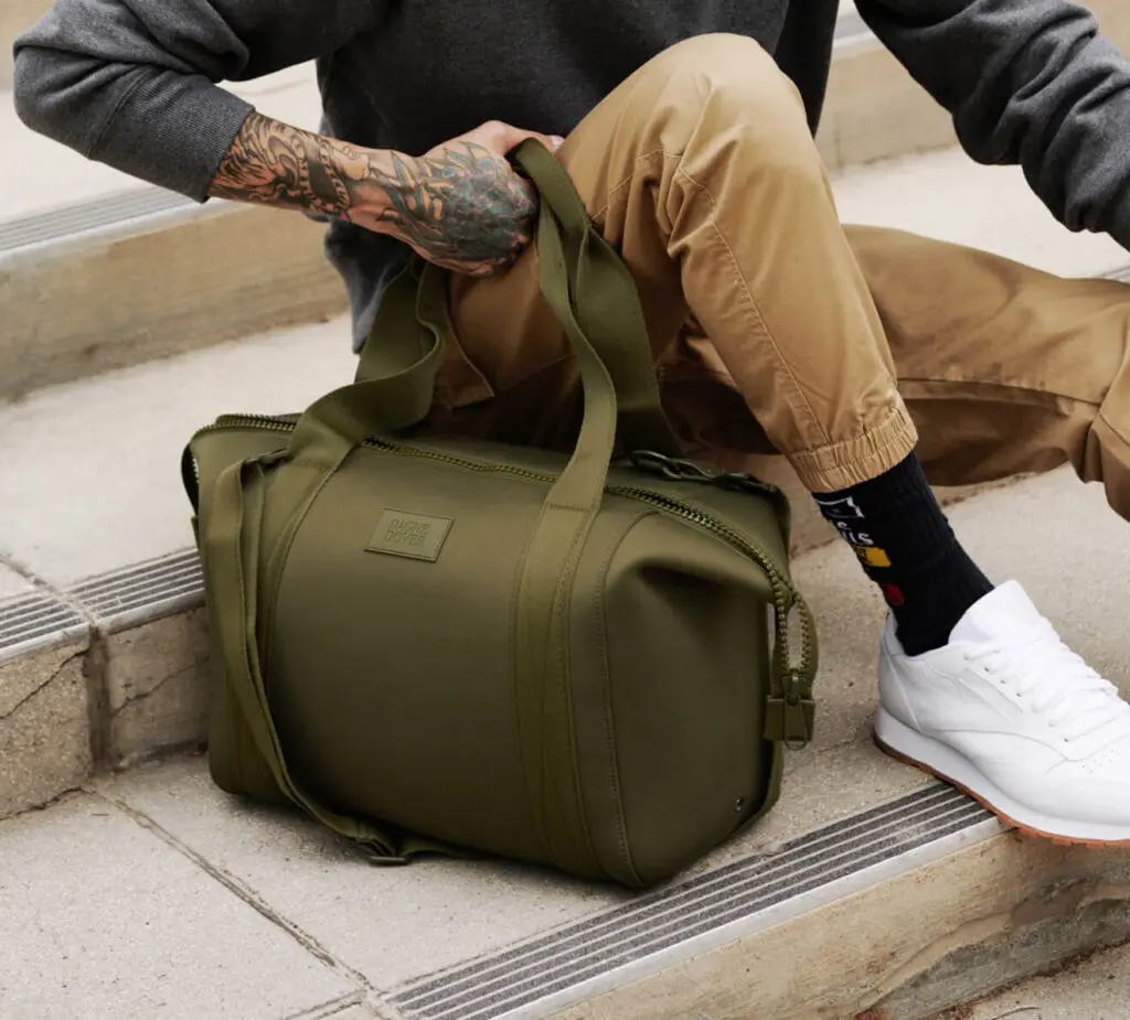 A man sitting on steps outside a building, holding a Dane Dover bag in his hand