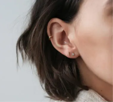 A close-up shot of an ear sporting a cartilage piercing and two stud earrings