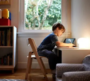 A young boy sits at a child-size desk and draws.