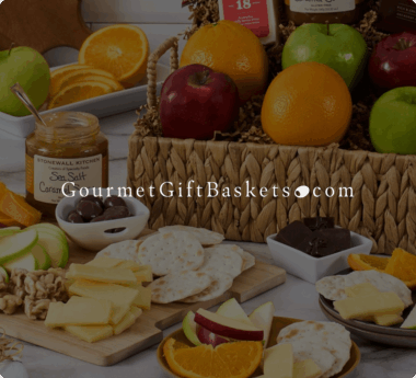 Assorted gourmet gift basket with apples, oranges, crackers, cheese, nuts, caramel sauce, and chocolate. GourmetGiftBaskets.com logo.