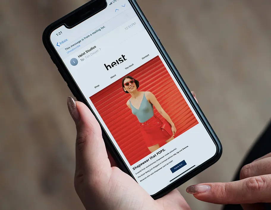 A hand holding a phone with an email campaign from Heist Studios on the phone screen.