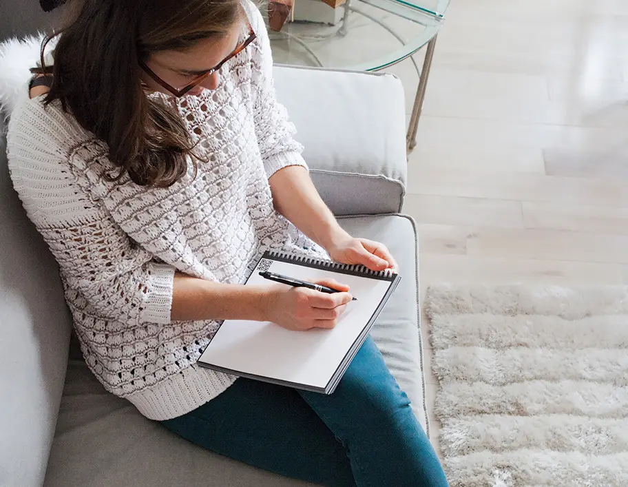 A woman sits and writes in a notebook while holding a pen.