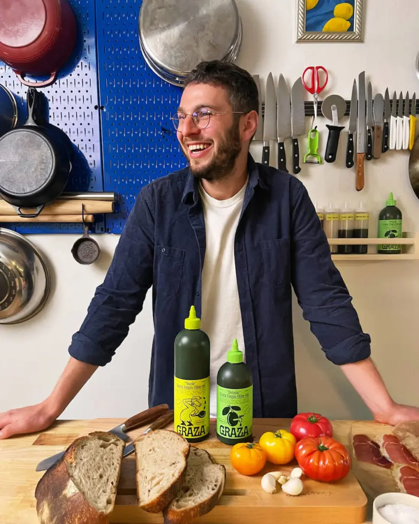 man smiling in front of olive oil bottles