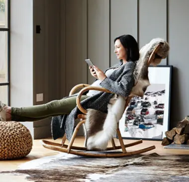 A woman in a rocking chair reading her tablet at home