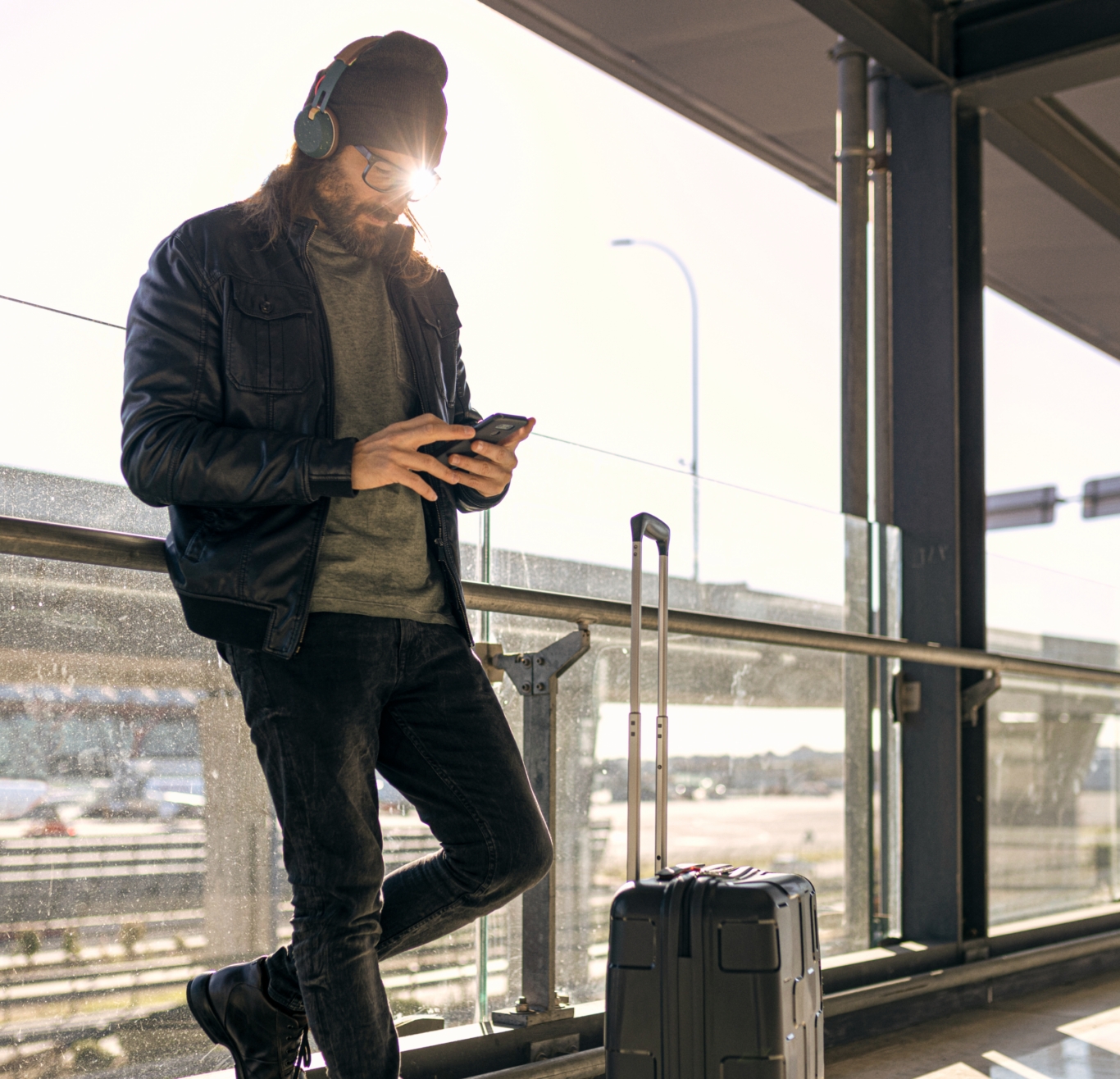 man leaning on a railing in the airport looking at his phone
