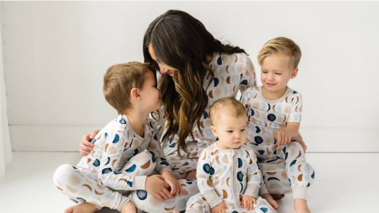 A woman wearing Little Sleepies brand pajamas is hugging three children, also dressed in Little Sleepies pajamas.