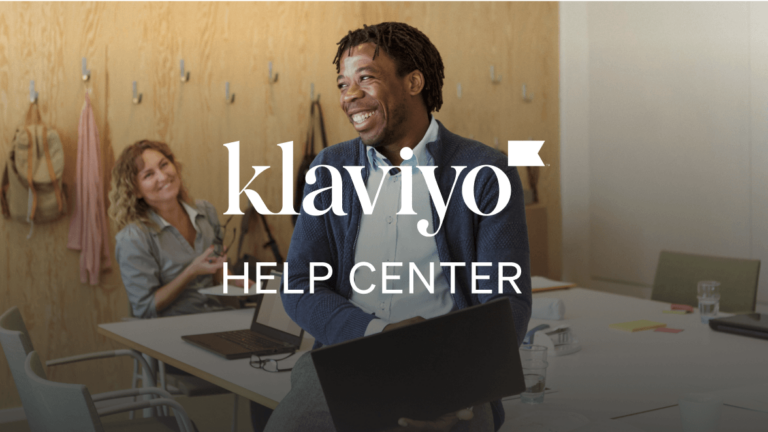 A photograph of man holding a laptop in a modern office space. He's leaning on a conference table and smiling. Text on top of the photo reads "Klaviyo help center."