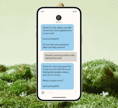 Smartphone displaying a text conversation about folic acid supplements with Stone Co. on a grassy background.