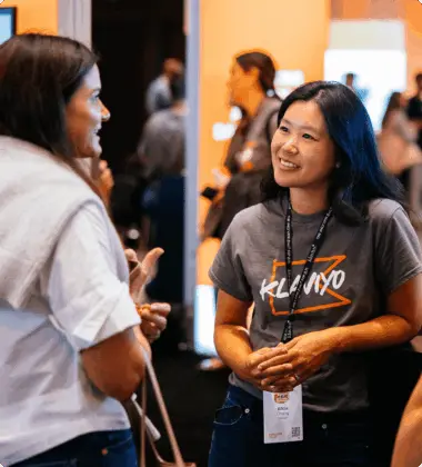 Two people talking at an event, one wearing a Klaviyo t-shirt and lanyard.
